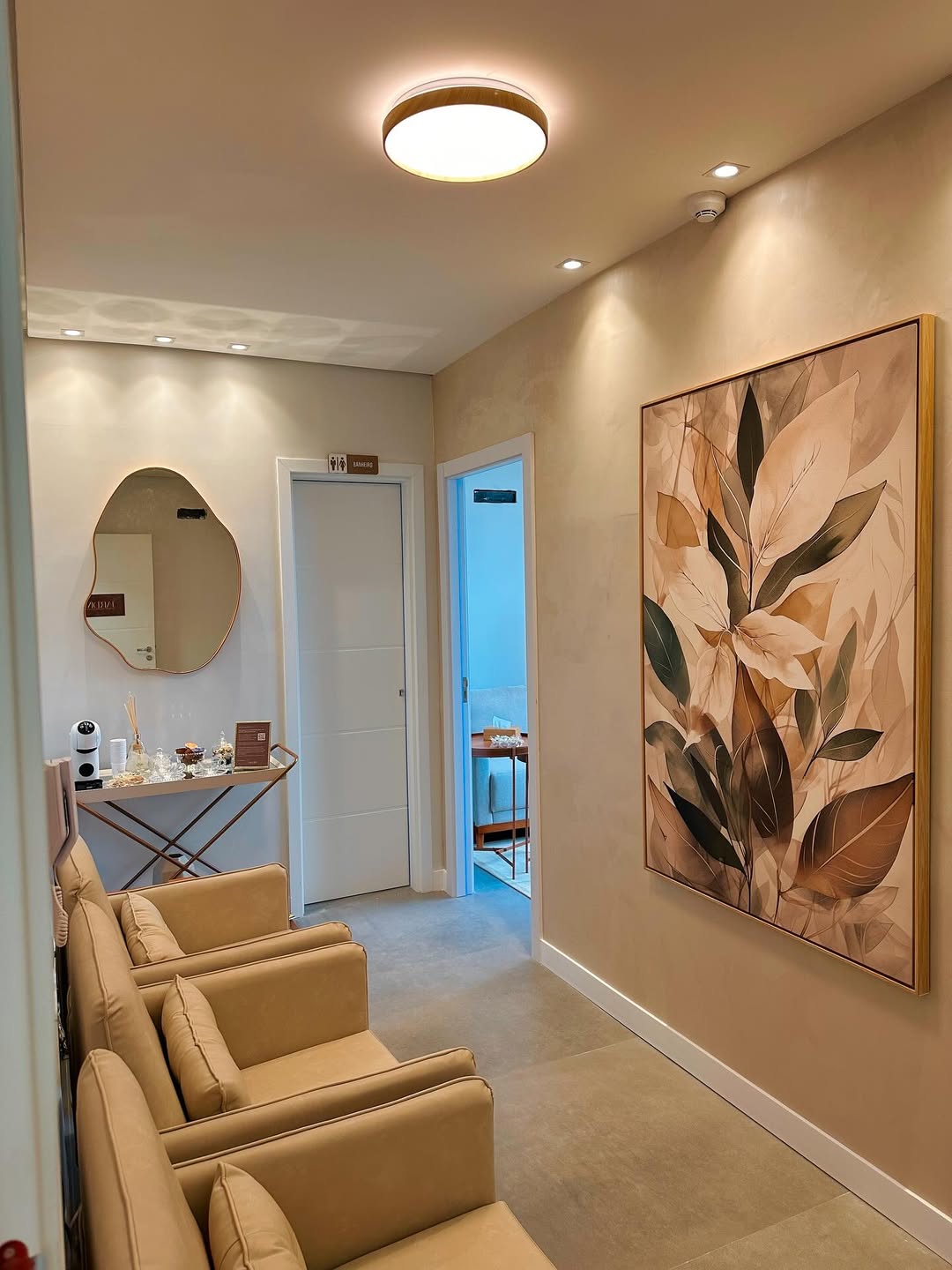 Recepção da Clínica Jardim, com poltronas bege, espelho dourado e quadro de folhas na parede.